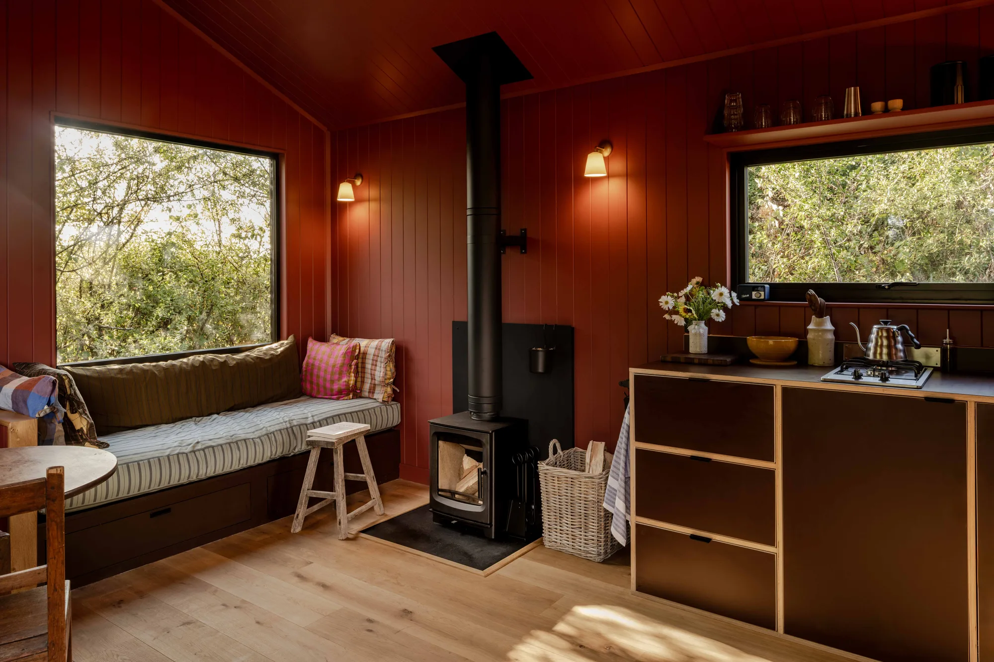 Inside a Shacks cabin lined in deep red: window seat, wood-burning stove and a compact kitchen