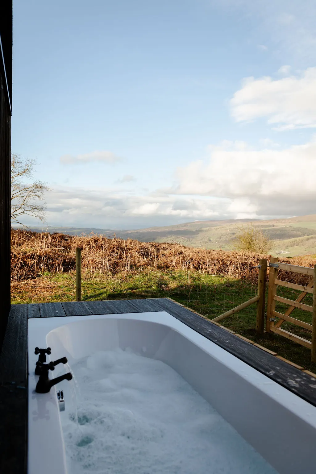 An outdoor bath on the Leo cabin deck overlooking open Welsh hills